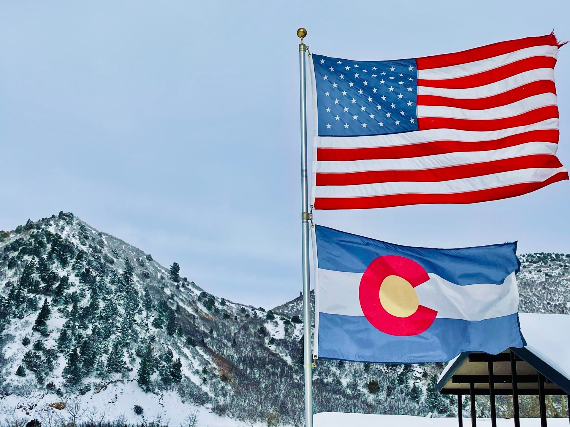 A United States flag above a Colorado state flag in front of a snowy hill. Photo by Fr. Daniel Ciucci